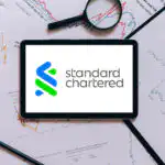 An iPad displaying the Standard Chartered logo surrounded by charts and graphs