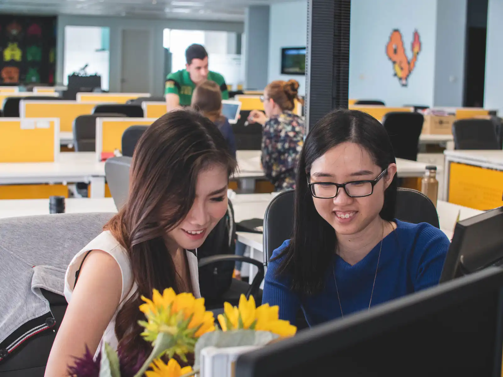 Two women in an office smiling and discussing what they see on their computer screen.