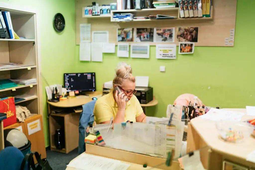 A health worker sitting in her office while holding the office phone in her right hand. She is trying to communicate to another person to relay important information.