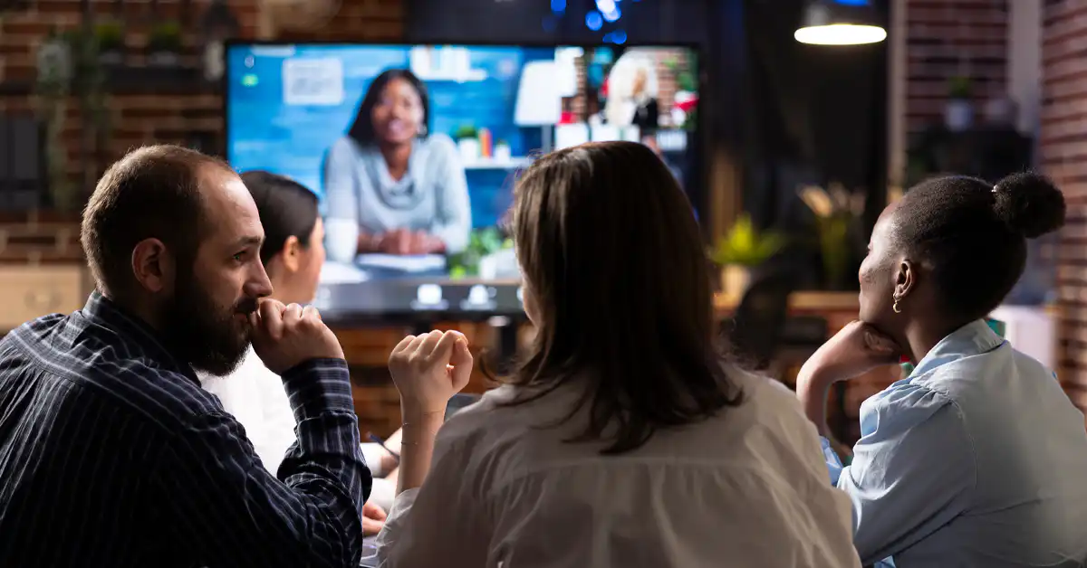 A photo of four colleagues having an online conference on a big screen with a female colleague