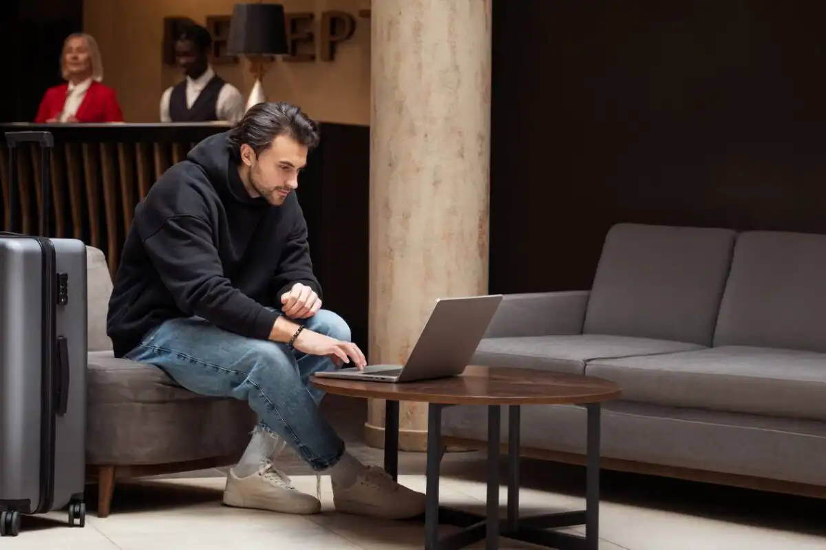 A modern traveler working on a laptop in a hotel lobby, illustrating how hybrid work influences current travel demand trends.